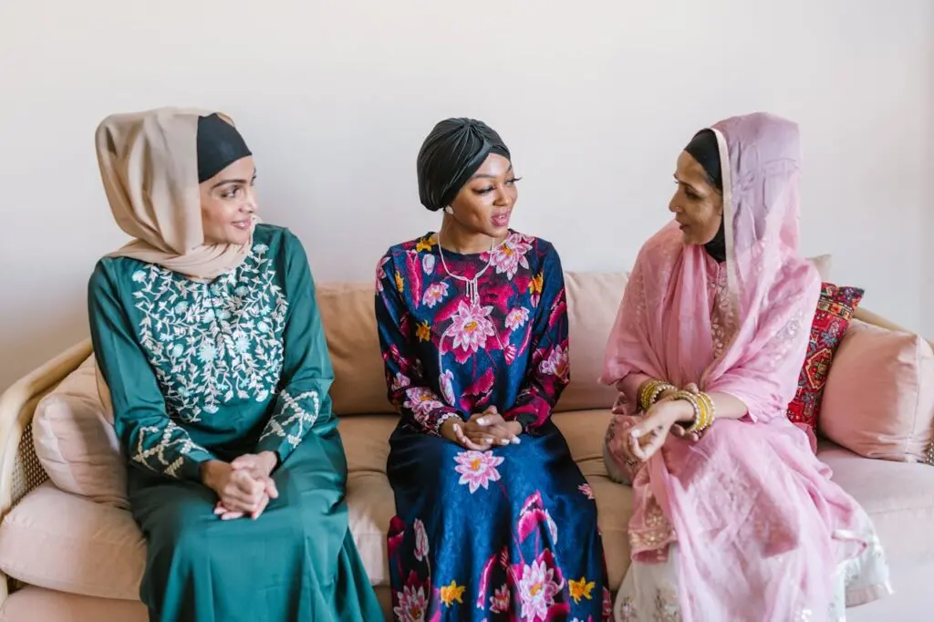 pexels-photo-7249337 Three women wearing traditional Islamic attire engaged in conversation indoors.